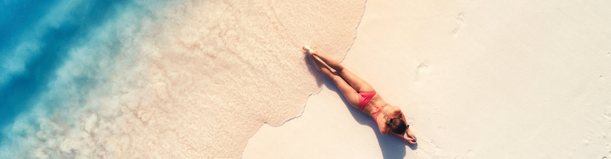 Person lying on a towel by a poolside with clear blue water